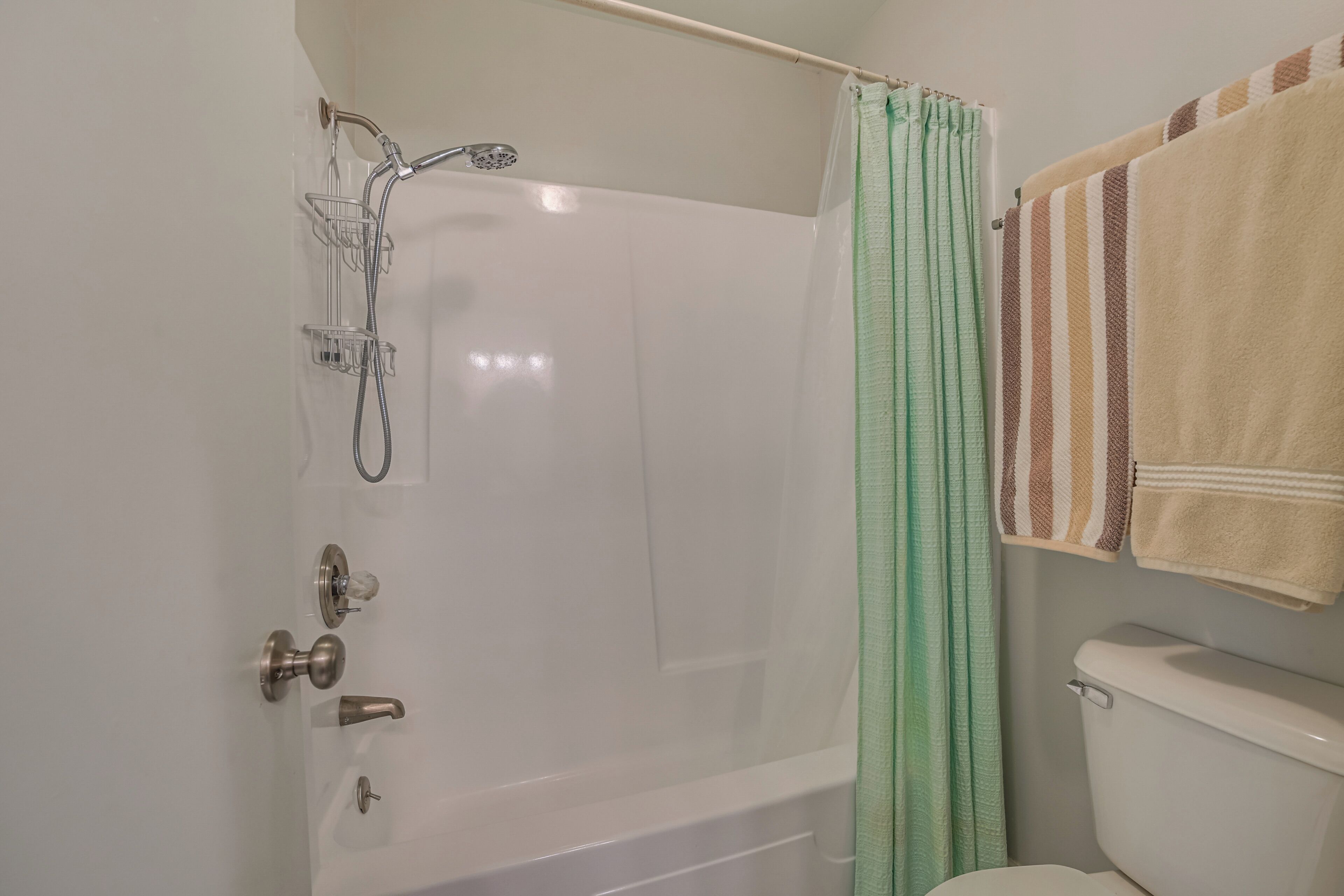 A bathroom with a white bathtub, a shower, a toilet, and a towel rack with striped towels.