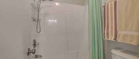 A bathroom with a white bathtub, a shower, a toilet, and a towel rack with striped towels.