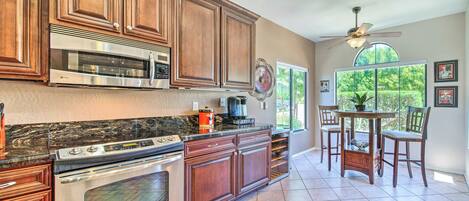 A kitchen with wooden cabinets, a built-in oven, a microwave, and a coffee maker. There is a dining table with chairs and a ceiling fan.