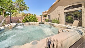 Un jacuzzi en un patio trasero con una pérgola, un porche cubierto y un muro de ladrillo.