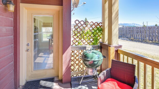 A covered porch with a door, a glass door, a wicker chair with a red cushion, and a green grill. - Walk to Main St! Ennis Townhome w/ Balcony (Ennis)
