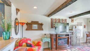 A cozy living room with a wooden bench, a colorful sofa, a vintage television, and a decorative birdcage. - Walk to Main St! Ennis Townhome w/ Balcony (Ennis)
