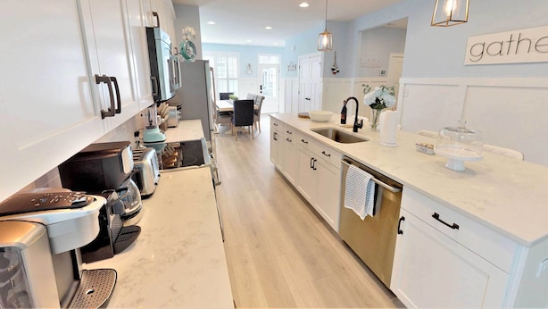 A modern kitchen with white cabinetry, a central island with a sink, and a dining area in the background. - 2 Mi to Bethany Beach: Family-friendly Home! (Ocean View)