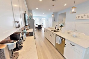 Een moderne keuken met witte kastjes, een centraal eiland met een spoelbak, en een eethoek op de achtergrond.