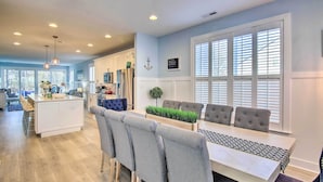 A modern kitchen with white cabinets, a dining area with grey upholstered chairs, and a large window with blinds. - 2 Mi to Bethany Beach: Family-friendly Home! (Ocean View)