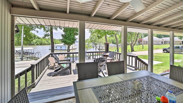 A covered outdoor deck with wicker furniture and a table, overlooking a lake and a dock area. - Dock & Grand Lake Access! Idyllic Afton Getaway (Afton)