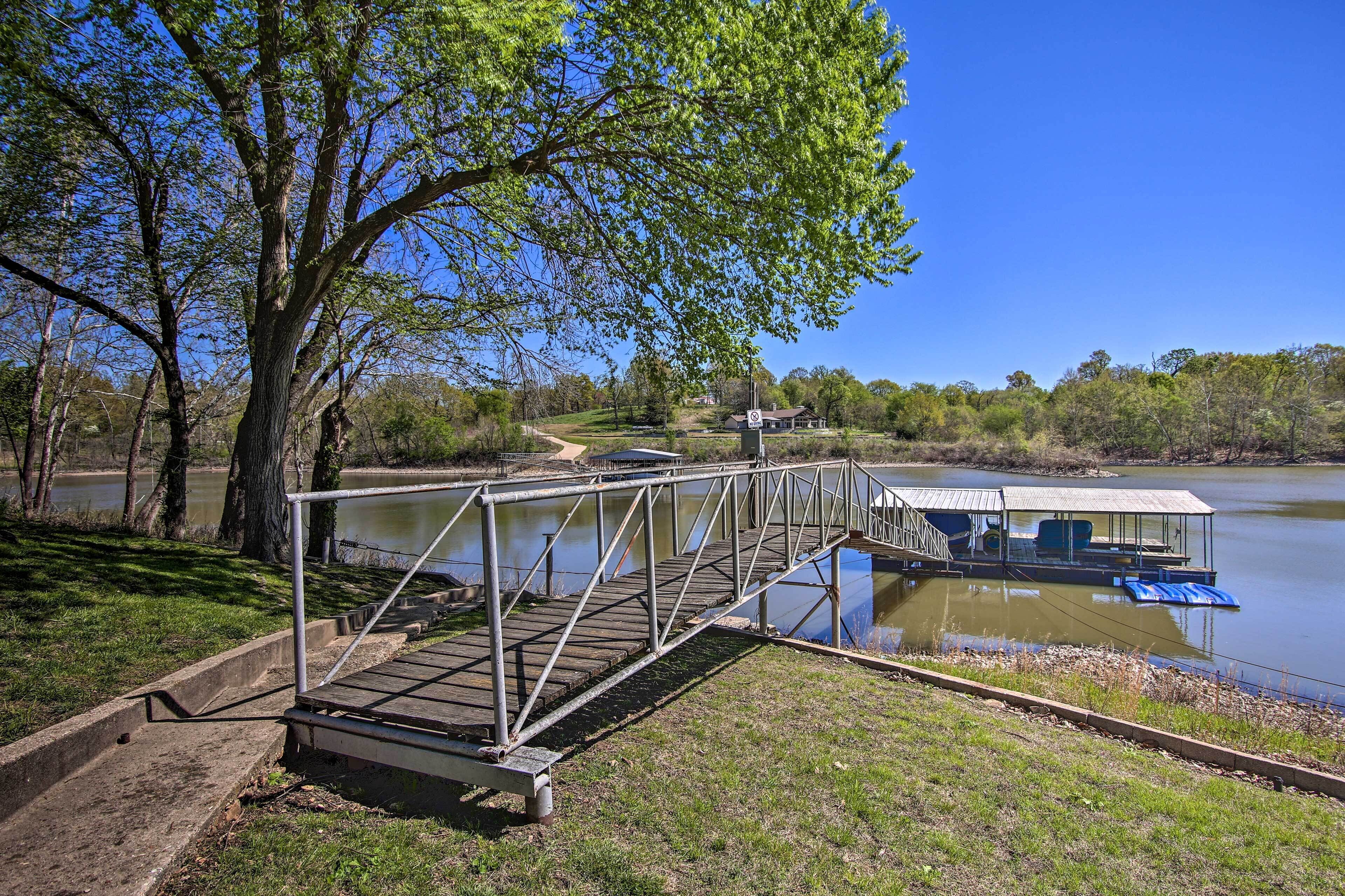 A wooden bridge leading to a covered dock by a calm lake, surrounded by trees and a clear sky.