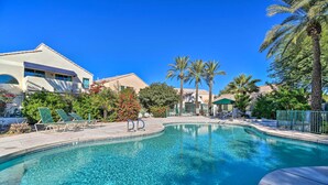Une piscine d’un bleu éclatant, avec des chaises longues, des palmiers et un bâtiment à la façade blanche.