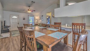 A spacious dining area with a large wooden table and matching chairs, a ceiling fan, and a kitchen area visible in the background. - Home 10 Mi to Downtown Pensacola: Pets Welcome! (Pensacola)