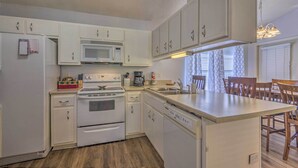 A compact kitchen with white cabinetry, a microwave, stove, and dishwasher. There is a small dining area with a table and chairs. - Home 10 Mi to Downtown Pensacola: Pets Welcome! (Pensacola)