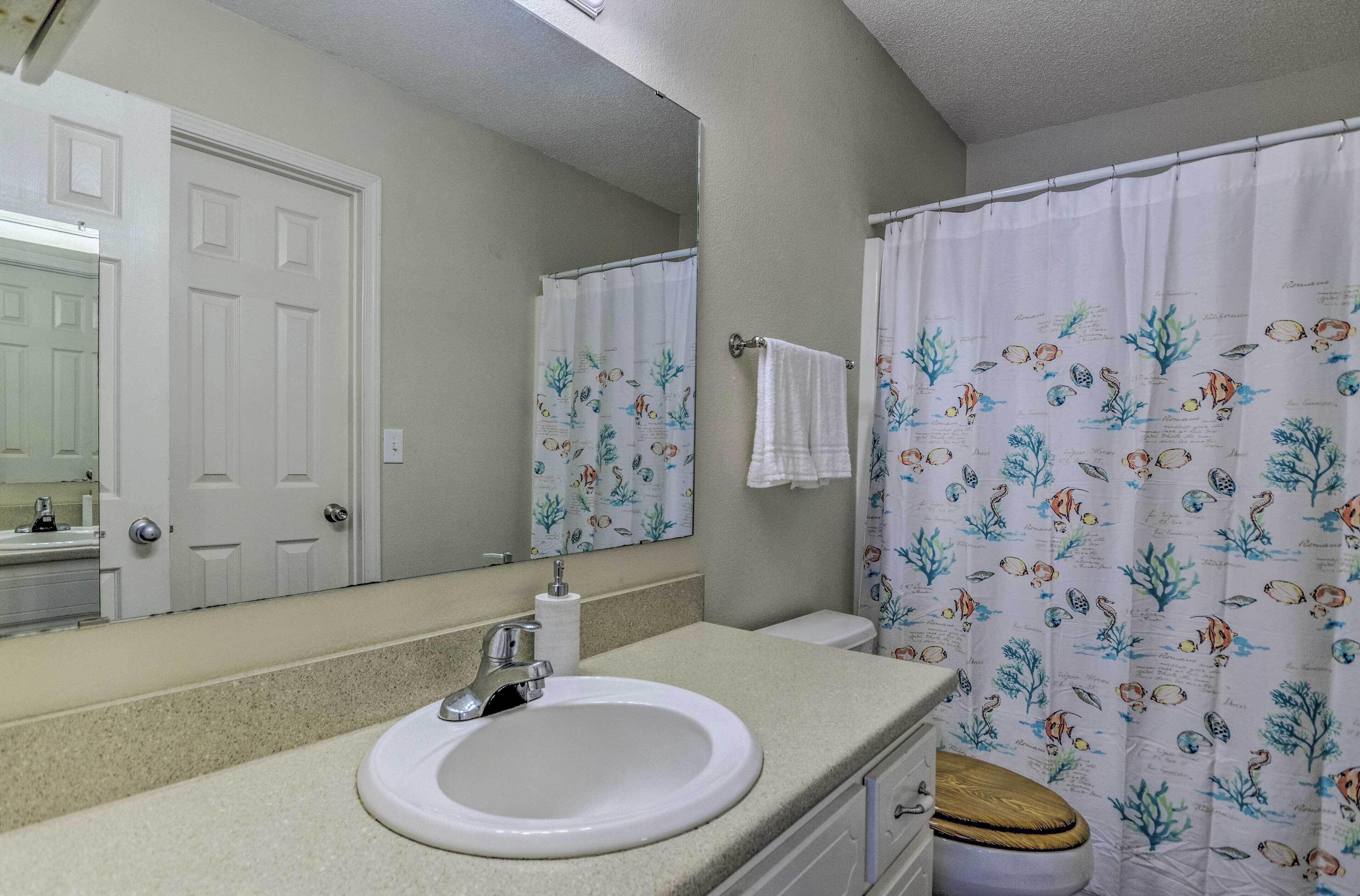 Une salle de bain avec un lavabo blanc, un miroir, des toilettes et un rideau de douche orné de motifs représentant la vie marine.