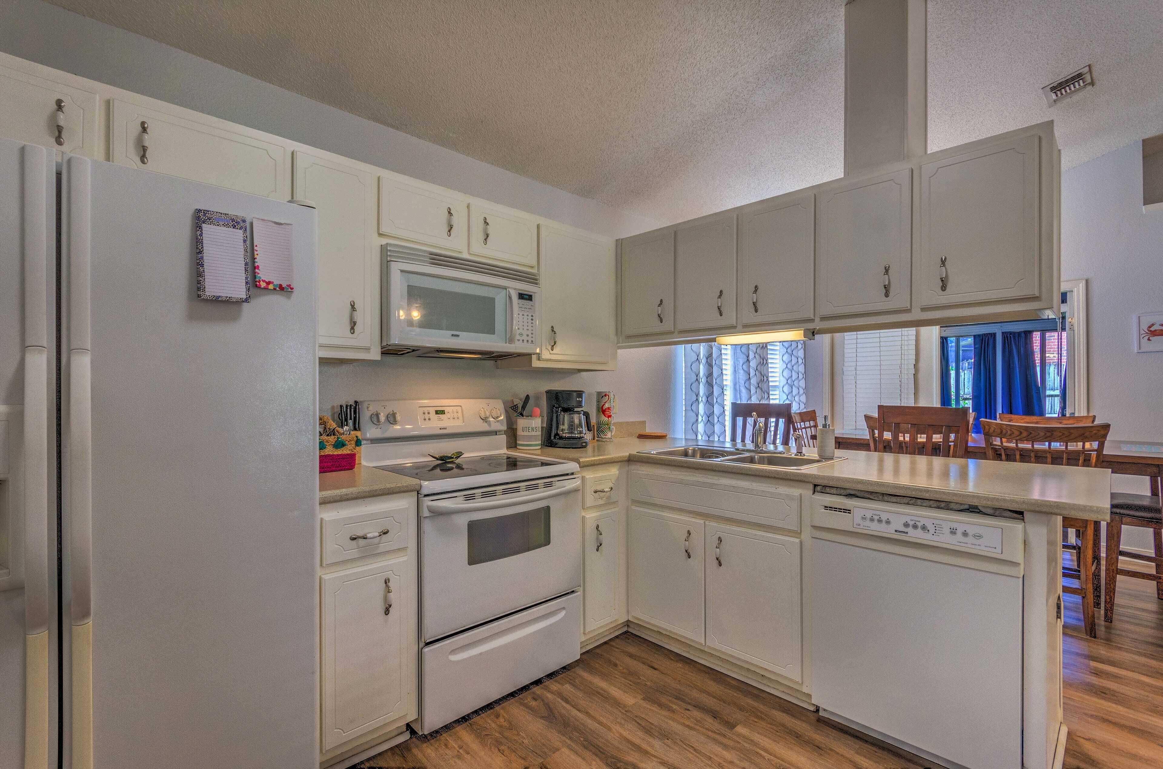 A kitchen with white cabinets, a microwave, an oven, and a dishwasher. There is a dining area with wooden chairs and a table.
