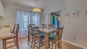A dining area with a wooden table and chairs, a chandelier, and a view of the outdoors through a window. - Home 10 Mi to Downtown Pensacola: Pets Welcome! (Pensacola)
