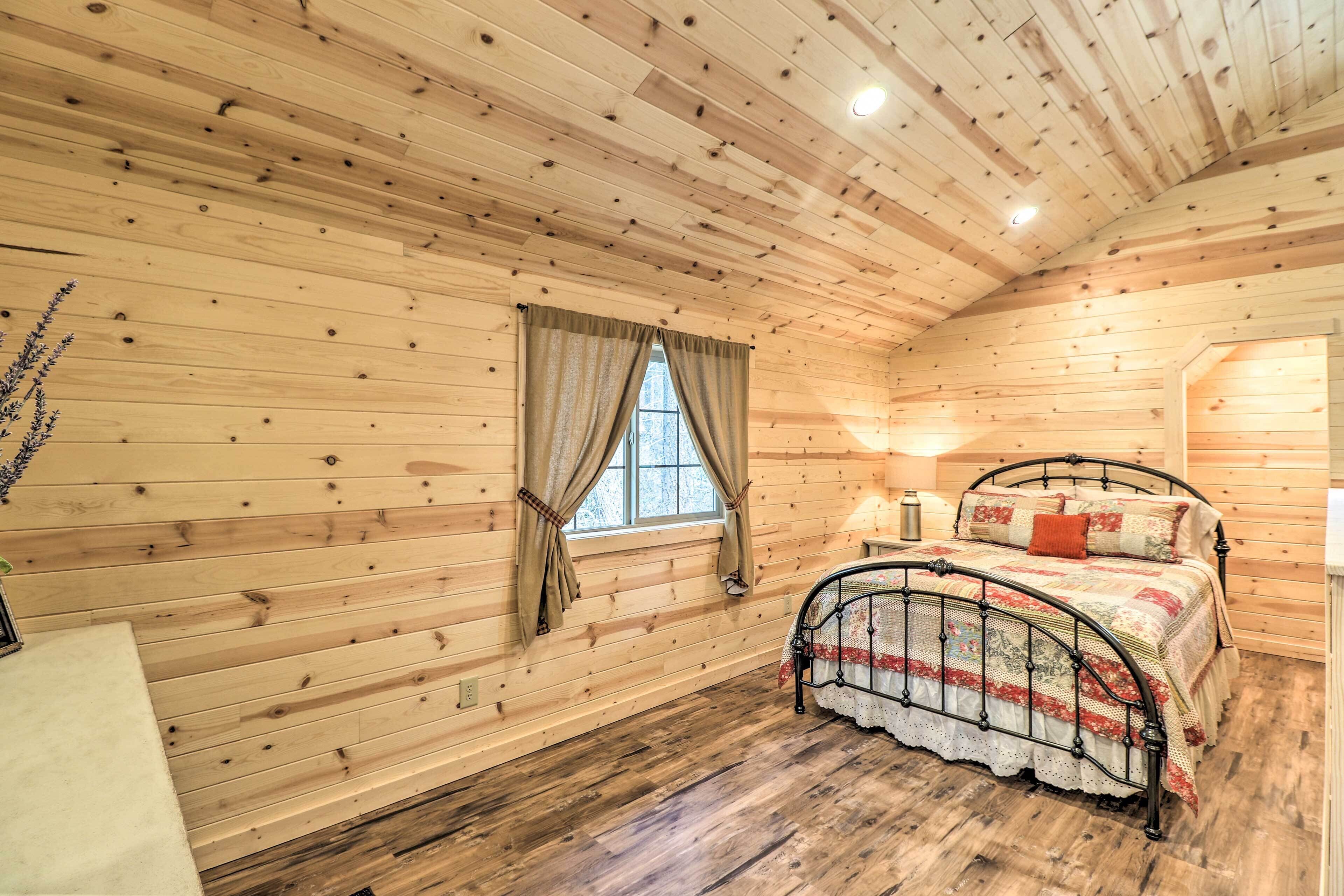 Un dormitorio de cabaña de madera con cama, una ventana con cortinas y una lámpara en el techo.
