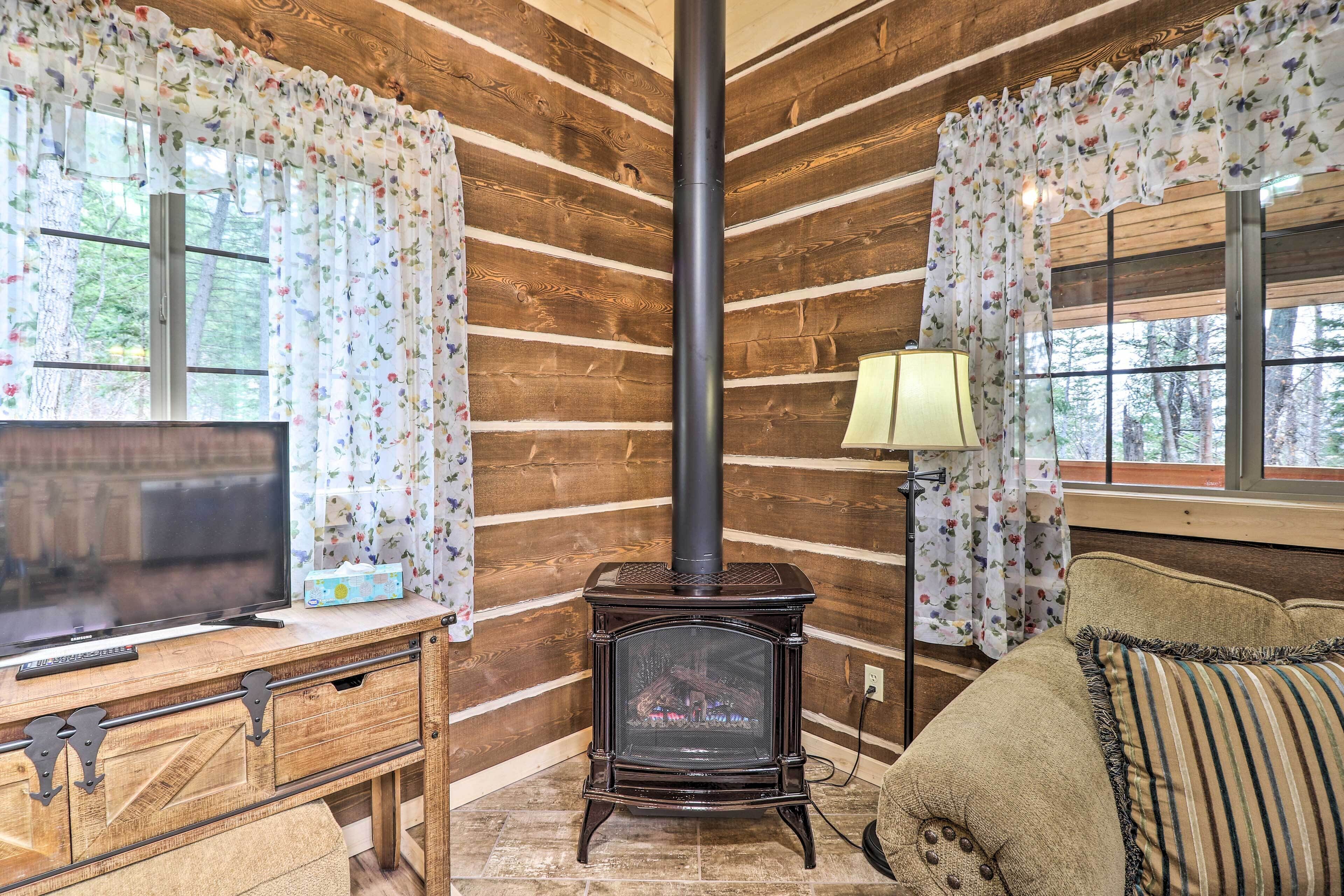 Interior acogedor de una cabaña con pared de madera, chimenea, televisor sobre un tocador de madera y sofá con un plaid estampado floral.