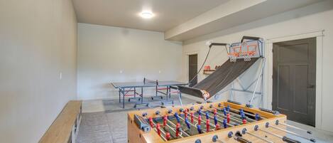 A foosball table, ping pong table, and a small basketball hoop in a room with a sloped ceiling.