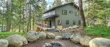 A cabin with a deck, surrounded by large rocks and a fire pit.