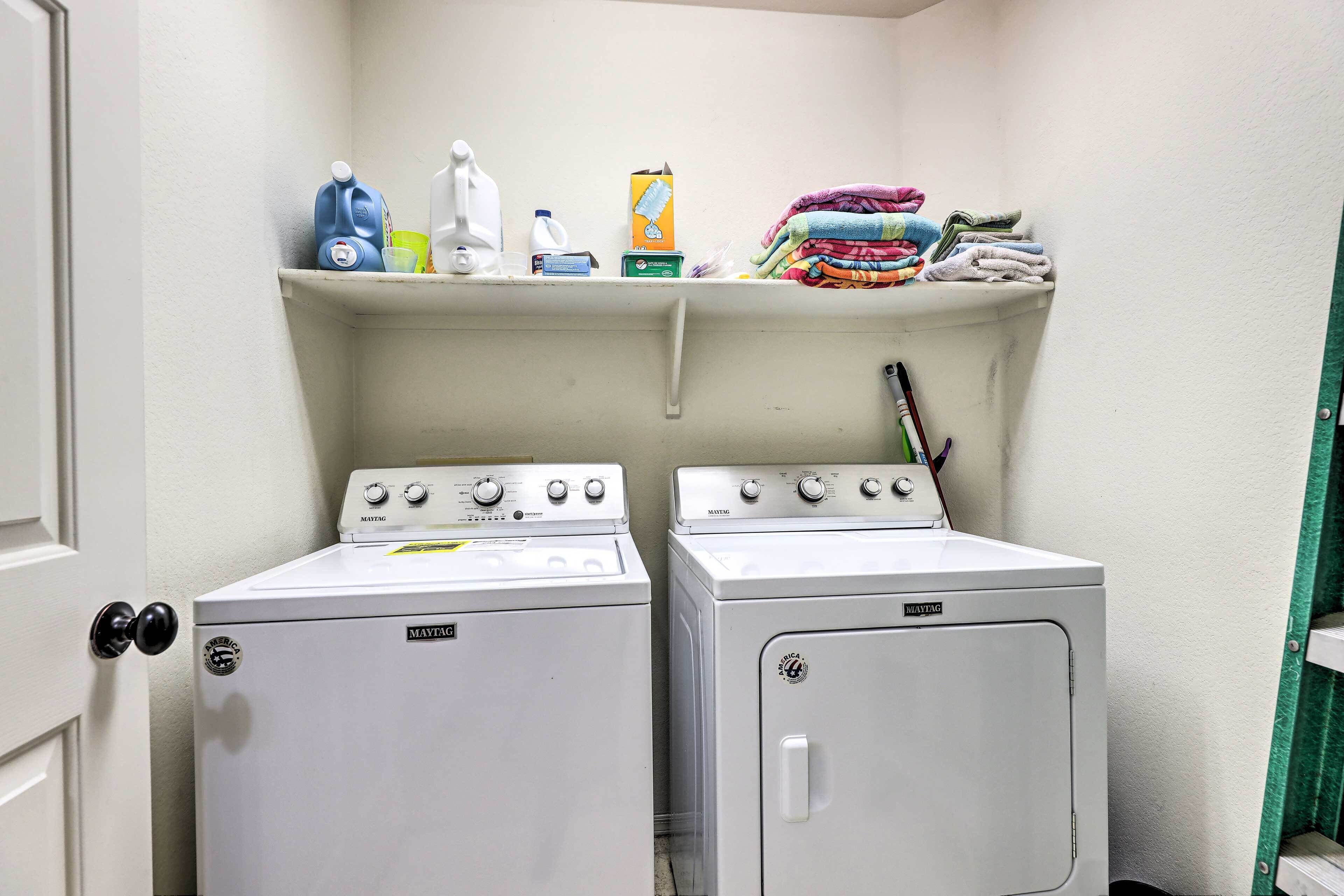 Un'area lavanderia con due lavatrici Maytag, uno scaffale con detersivi e un'anta con pomello nero.