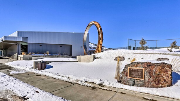 A modern building with a large metal arch structure in front. - Beauty in the Black Hills: An Upscale Apt. in Lead (Lead)