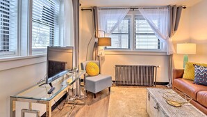 A living room with a glass coffee table, a leather sofa, a grey armchair with a yellow cushion, a floor lamp, and a radiator. - Beauty in the Black Hills: An Upscale Apt. in Lead (Lead)