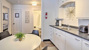 A modern kitchen with white cabinets, a black countertop, and a coffee maker. There is a dining table with chairs and a potted plant. - Beauty in the Black Hills: An Upscale Apt. in Lead (Lead)