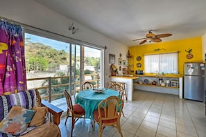 A dining area with a table and chairs, a kitchen with a refrigerator, and a balcony with a view of greenery. - Sayulita Condo: Walk to Beach, Plaza & Dining! (Sayulita)