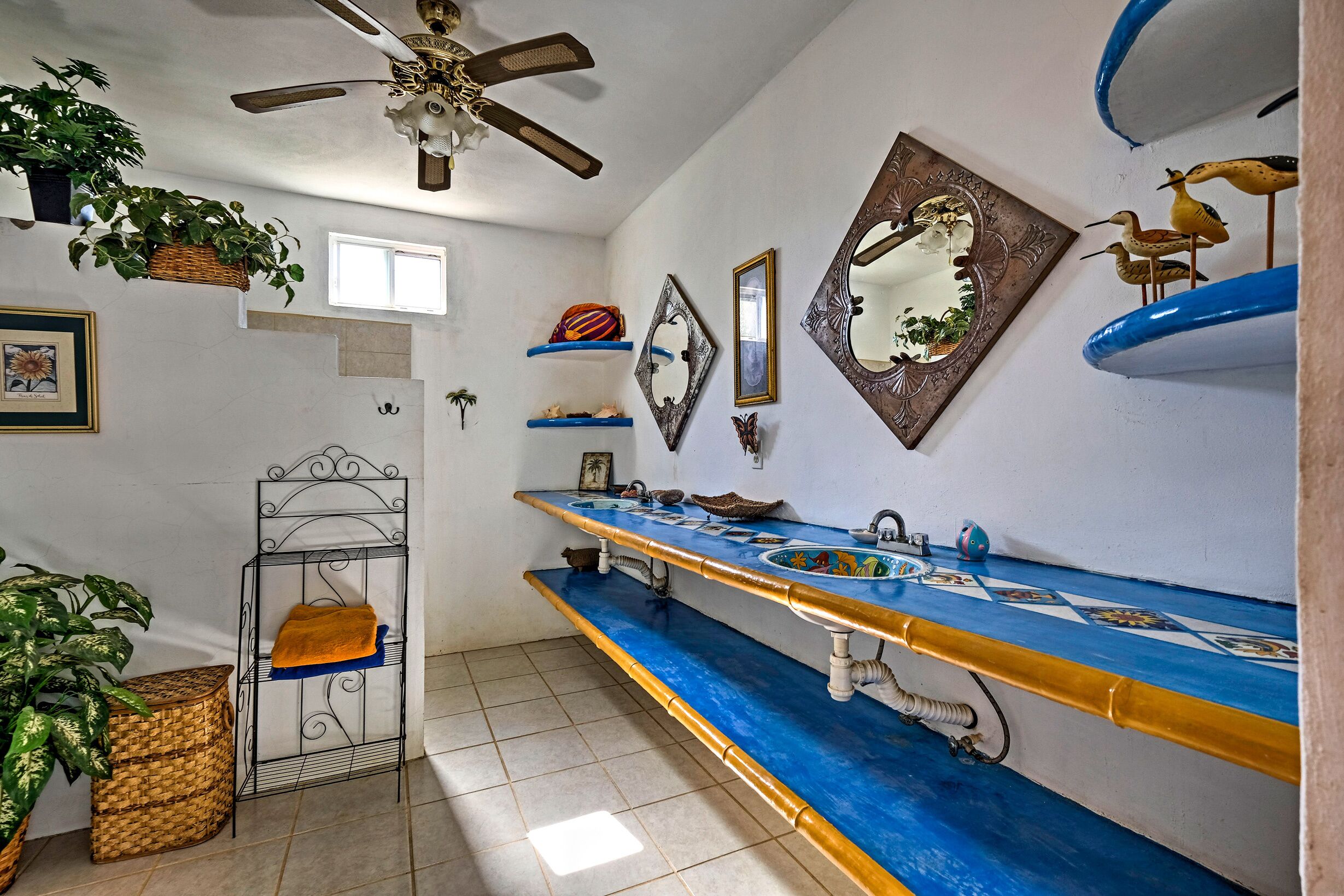 Une salle de bain avec un meuble-lavabo bleu, un ventilateur de plafond et des miroirs décoratifs.