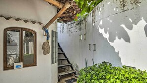 A narrow courtyard with a wooden staircase leading to a second floor, a small window with a sign, and a wall with a textured pattern. - Sayulita Condo: Walk to Beach, Plaza & Dining! (Sayulita)