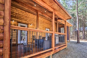 A wooden cabin with a porch, outdoor seating, and a gravel ground. - 'the Breeze' - Broken Bow Cabin w/ Hot Tub & Deck! (Broken Bow)