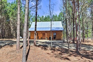 A log cabin with a metal roof, surrounded by tall pine trees. - 'the Breeze' - Broken Bow Cabin w/ Hot Tub & Deck! (Broken Bow)