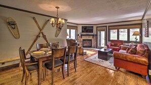 A spacious living room with a fireplace, wooden flooring, a dining area with chairs and a table, and a red sofa. - Brian Head Condo w/ Patio & Community Amenities! (Brian Head)