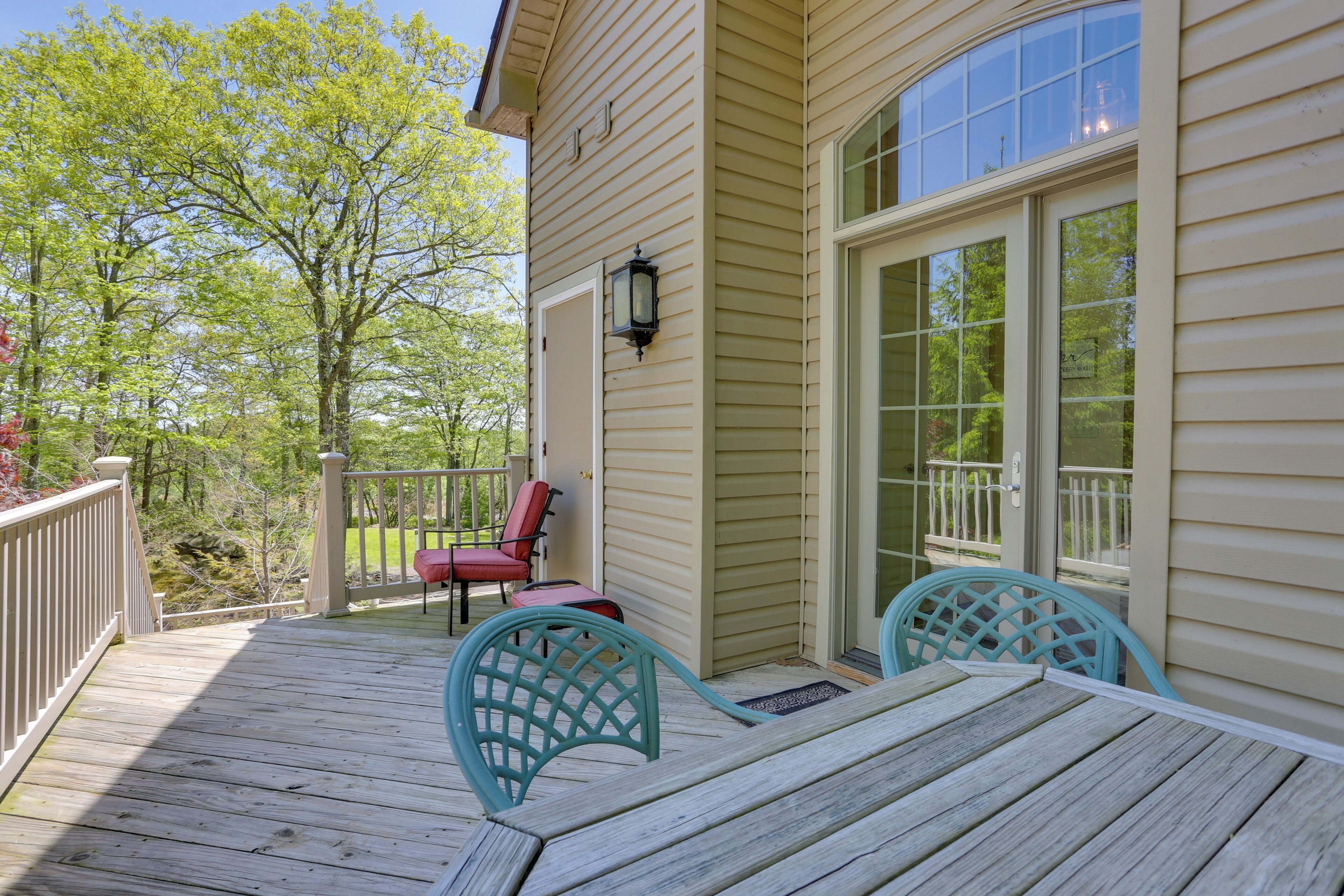 A wooden deck with two chairs and a table, a red chair, and a glass door leading to a balcony.