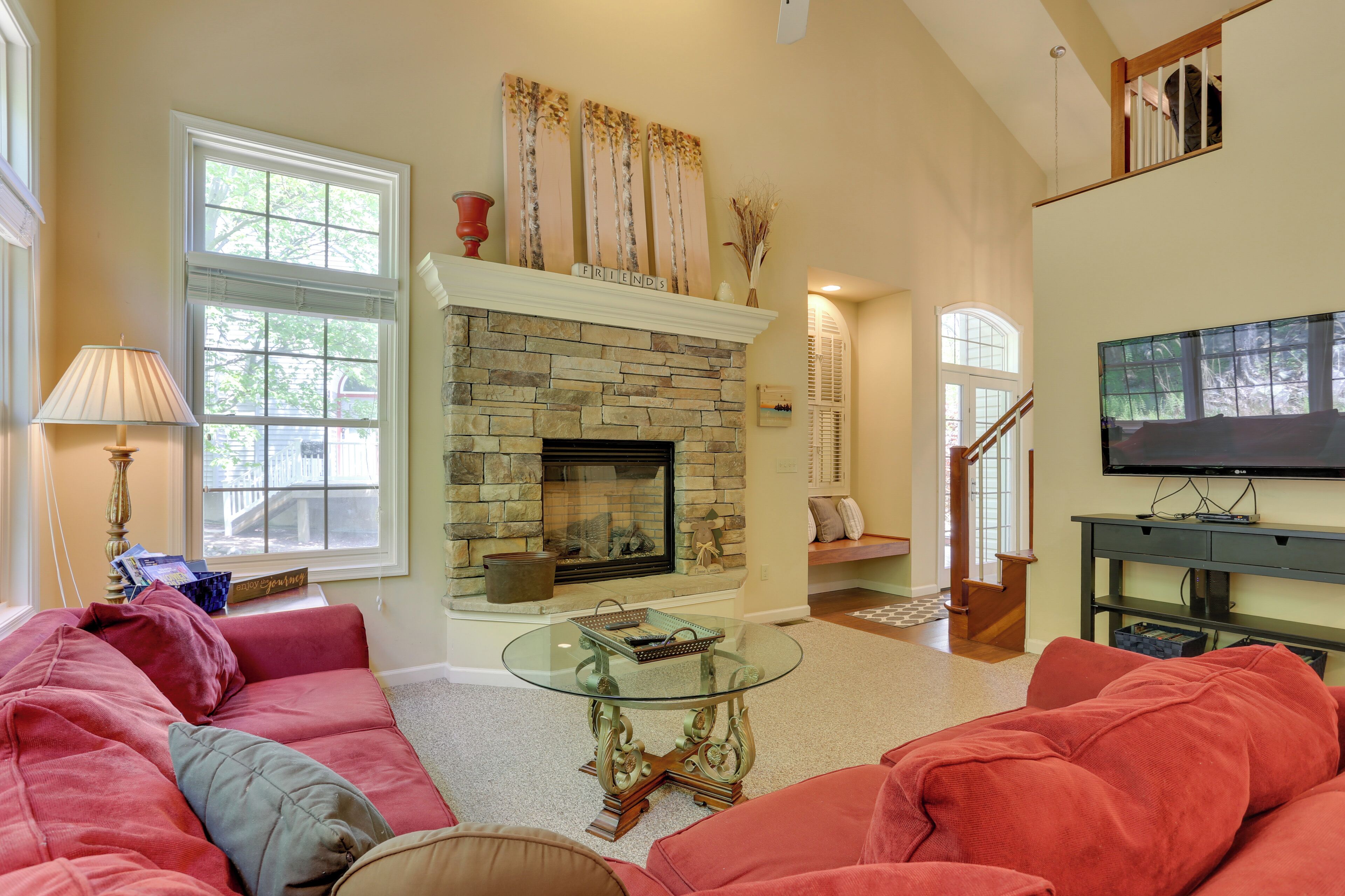 A living room with a stone fireplace, a glass coffee table, and a red sofa.