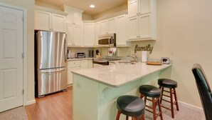A kitchen with white cabinets, stainless steel appliances, a central island with stools, and a 'family' sign.