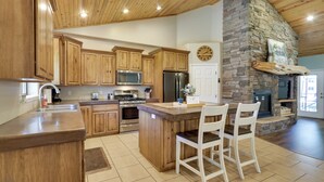 A spacious kitchen with wooden cabinets, a central island, and a stone fireplace. - Modern Show Low Home w/ BBQ & Fire Pit! (Show Low)