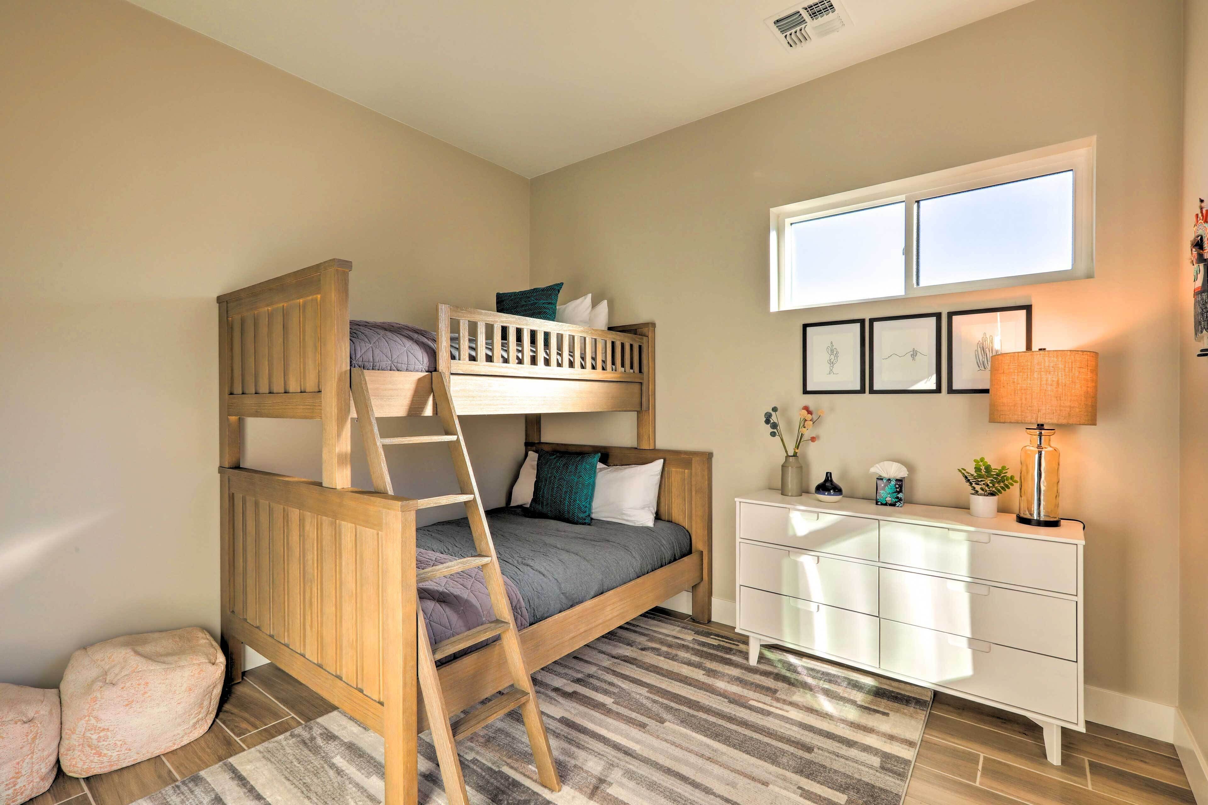 A bunk bed with a ladder, a white dresser, a window with blinds, and a rug.