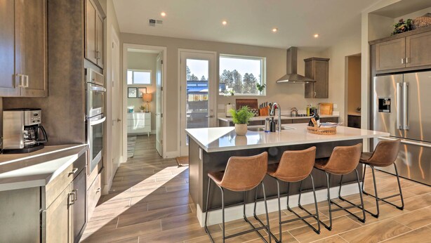 A modern kitchen with a large island, bar stools, stainless steel appliances, and a view of the outdoors. - Flagstaff Home w/ Patios + Mount Humphries Views! (Flagstaff)
