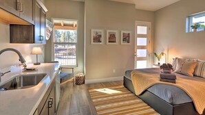 A modern kitchen with a sink, cabinets, and a window. There is a bed with a blanket and pillows, and a small rug on the floor. - Flagstaff Home w/ Patios + Mount Humphries Views! (Flagstaff)