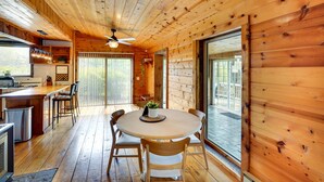 A wooden cabin interior with a dining area, kitchen, and large sliding glass doors leading to a deck. - New York Vacation Rental w/ Large Deck! (Saugerties)