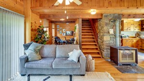 A cozy living room with a grey sofa, a ceiling fan, and a stone fireplace. - New York Vacation Rental w/ Large Deck! (Saugerties)
