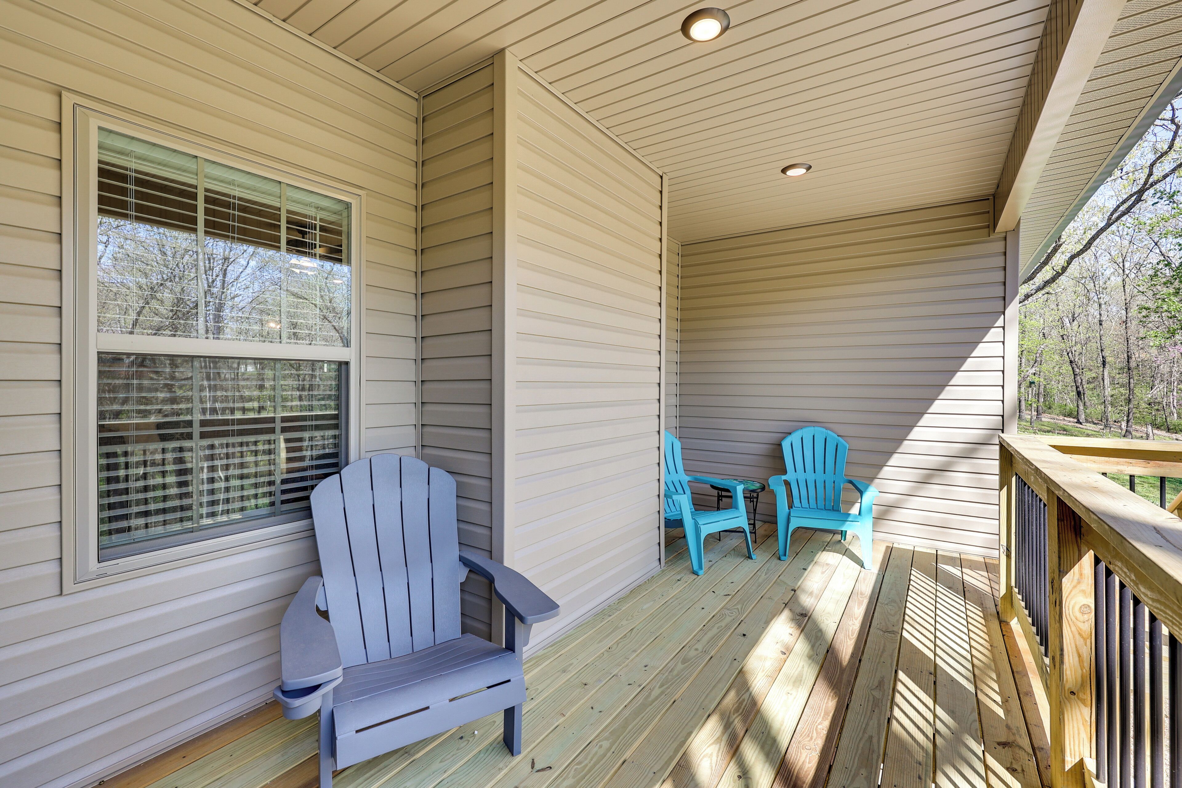 A covered porch with wooden railings, two Adirondack chairs, and a window with blinds.