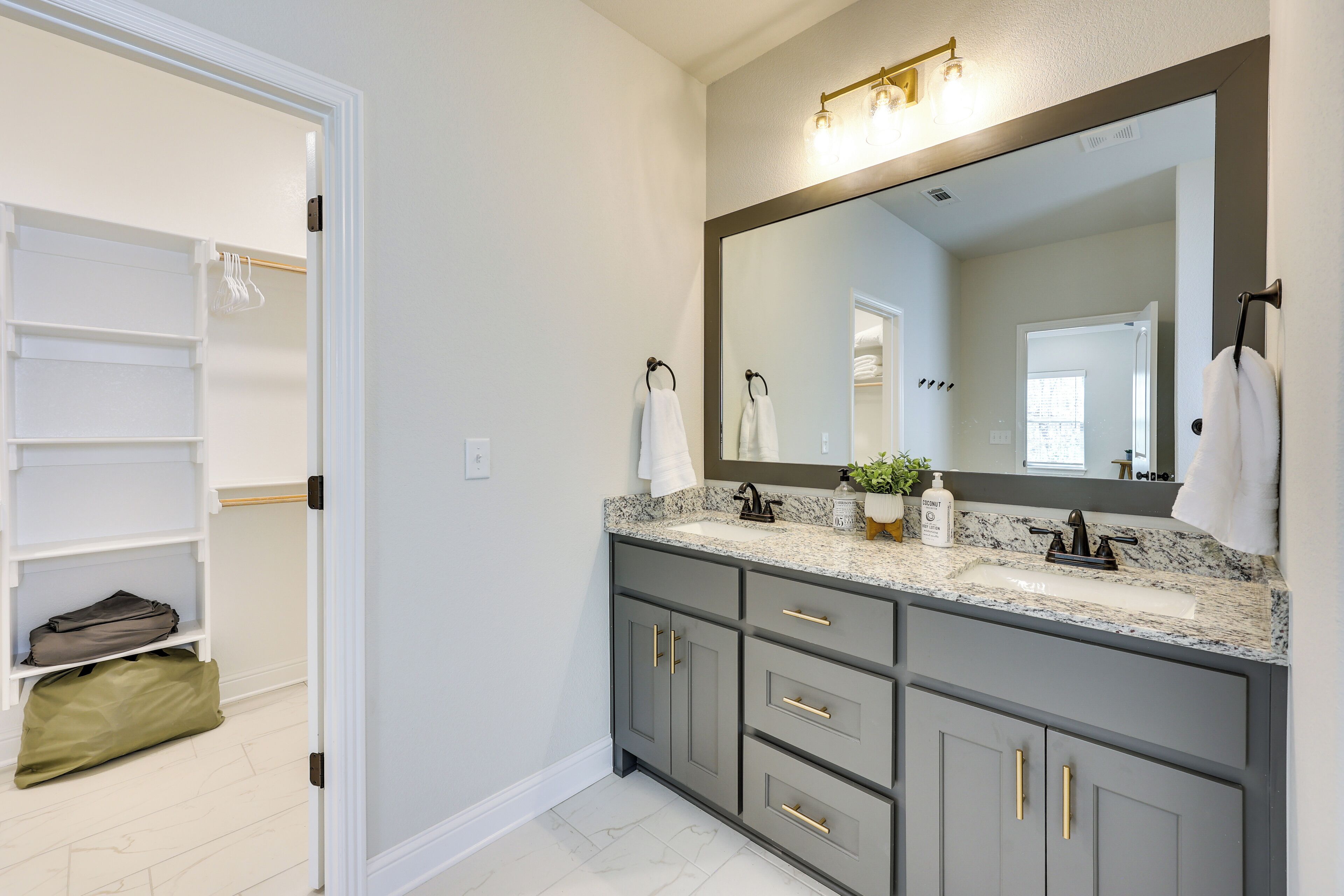 A bathroom with a large mirror, two sinks, and a walk-in closet with shelves and hanging space.