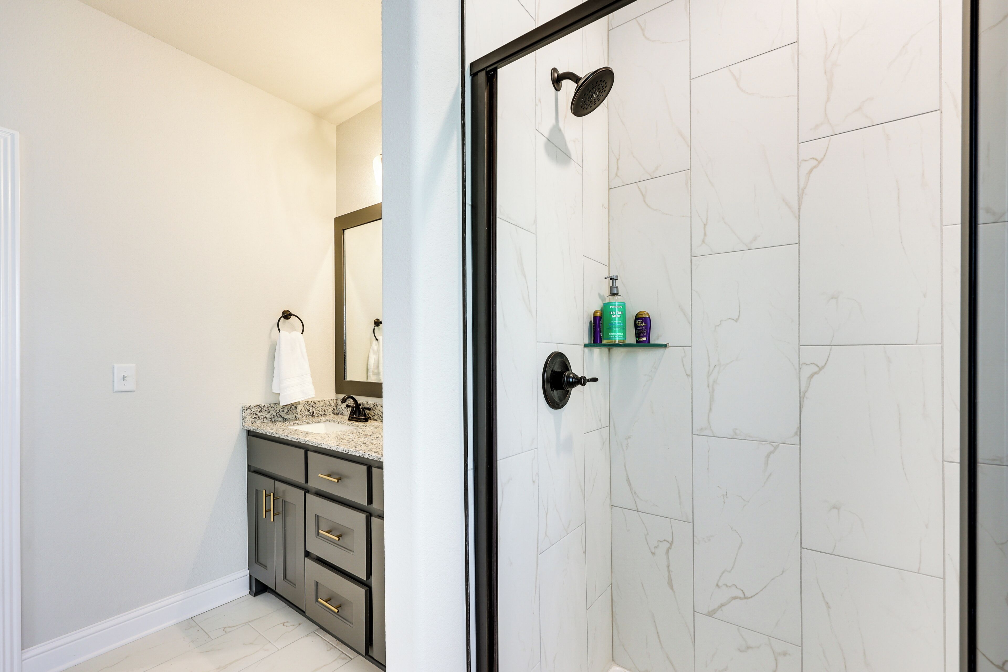 A bathroom with a shower, a vanity with a mirror, and a towel hanging on a rack.