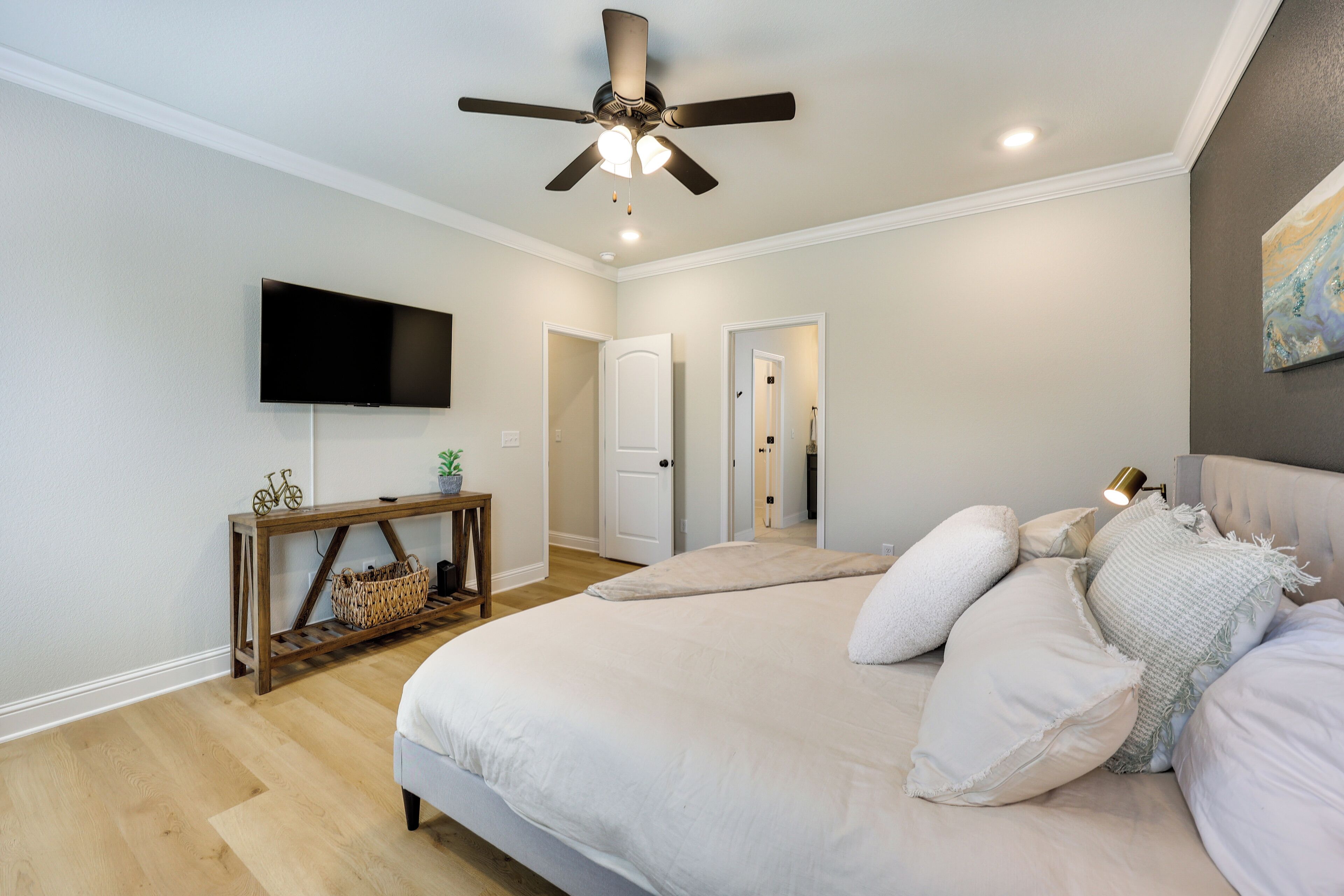 A bedroom with a bed, a ceiling fan, a TV, and a console table with a basket.