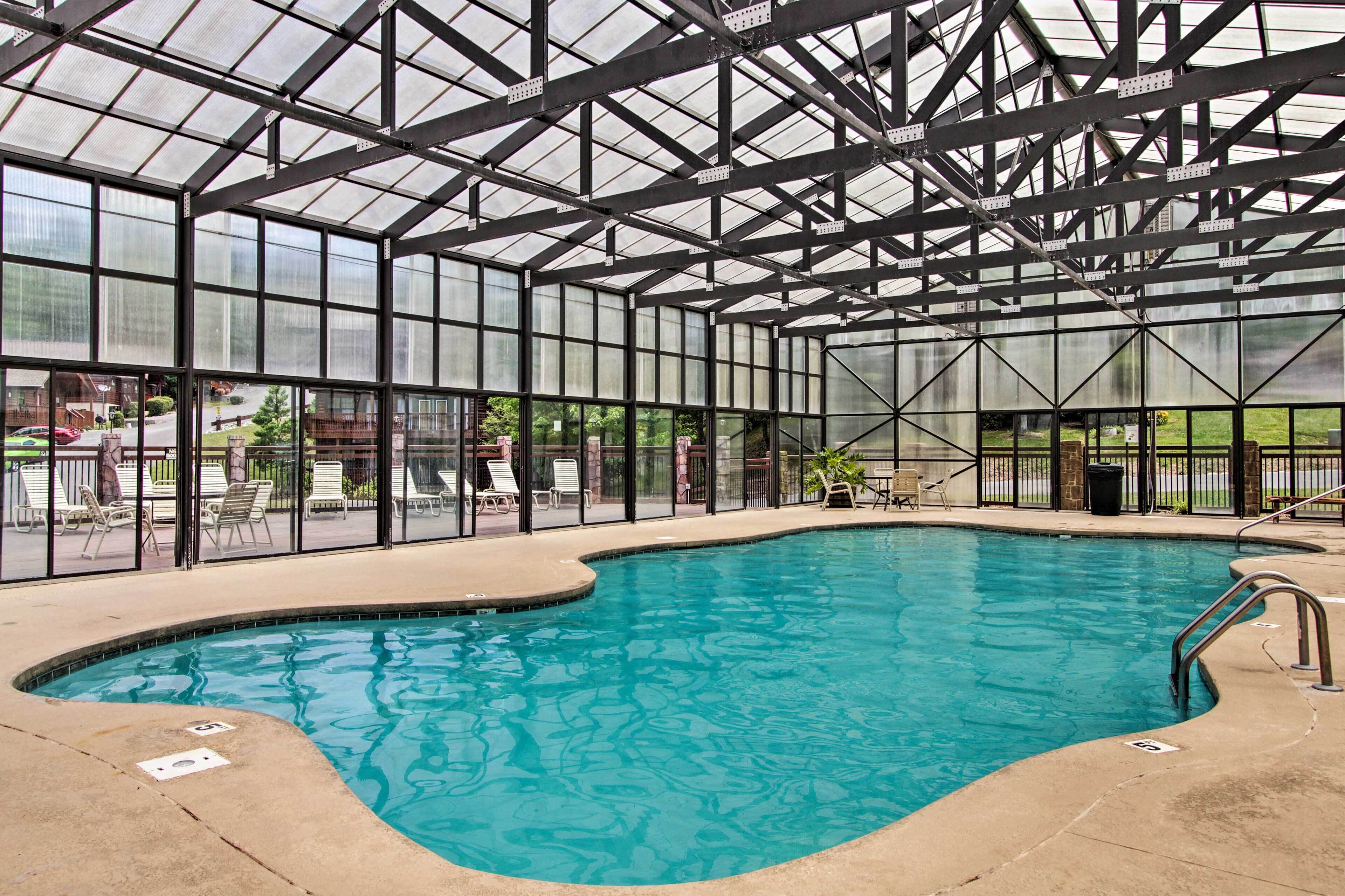 A large indoor swimming pool with a glass ceiling, surrounded by lounge chairs and a view of the outside.