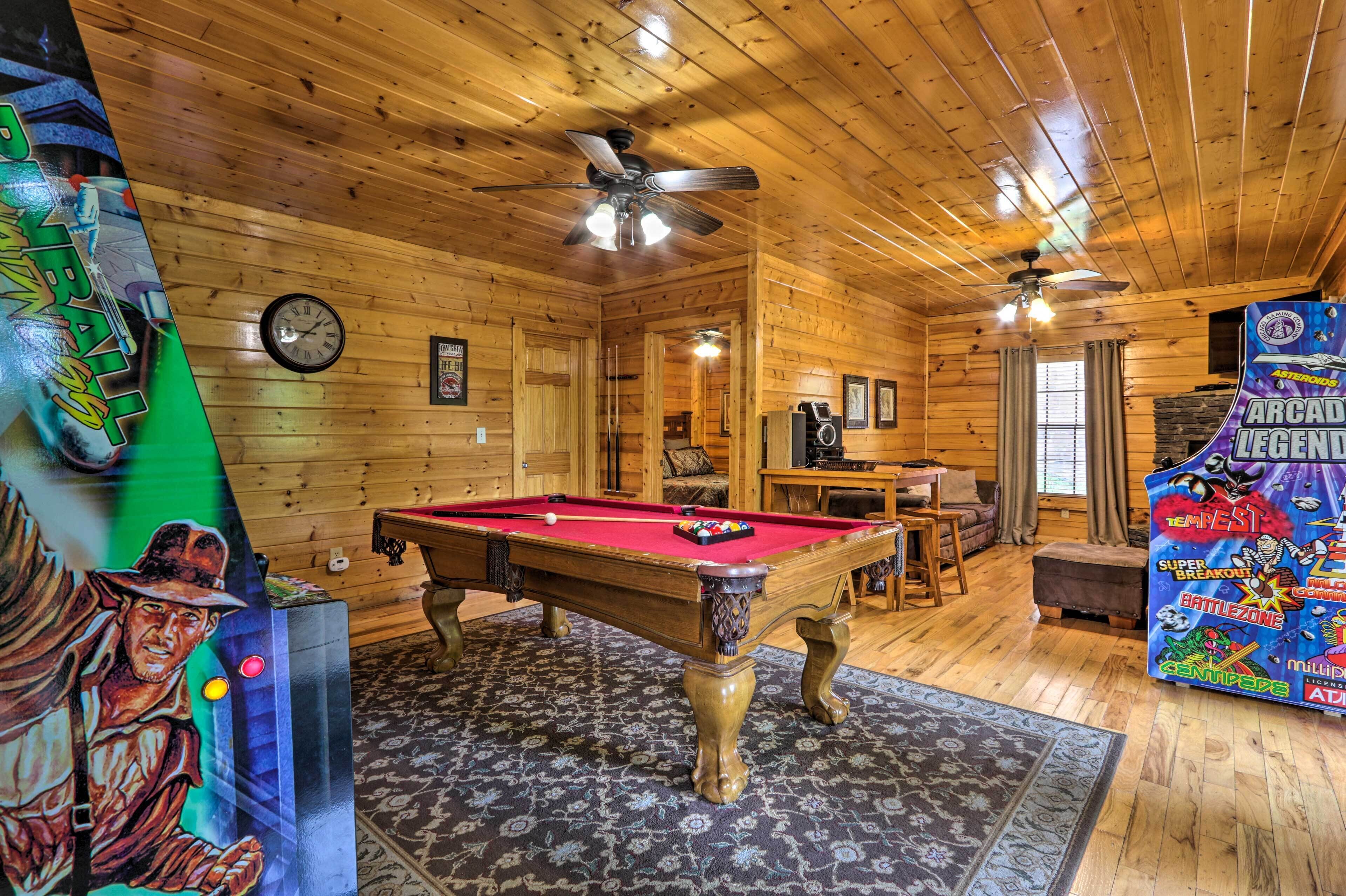 A wooden interior with a pool table, ceiling fans, and arcade game.
