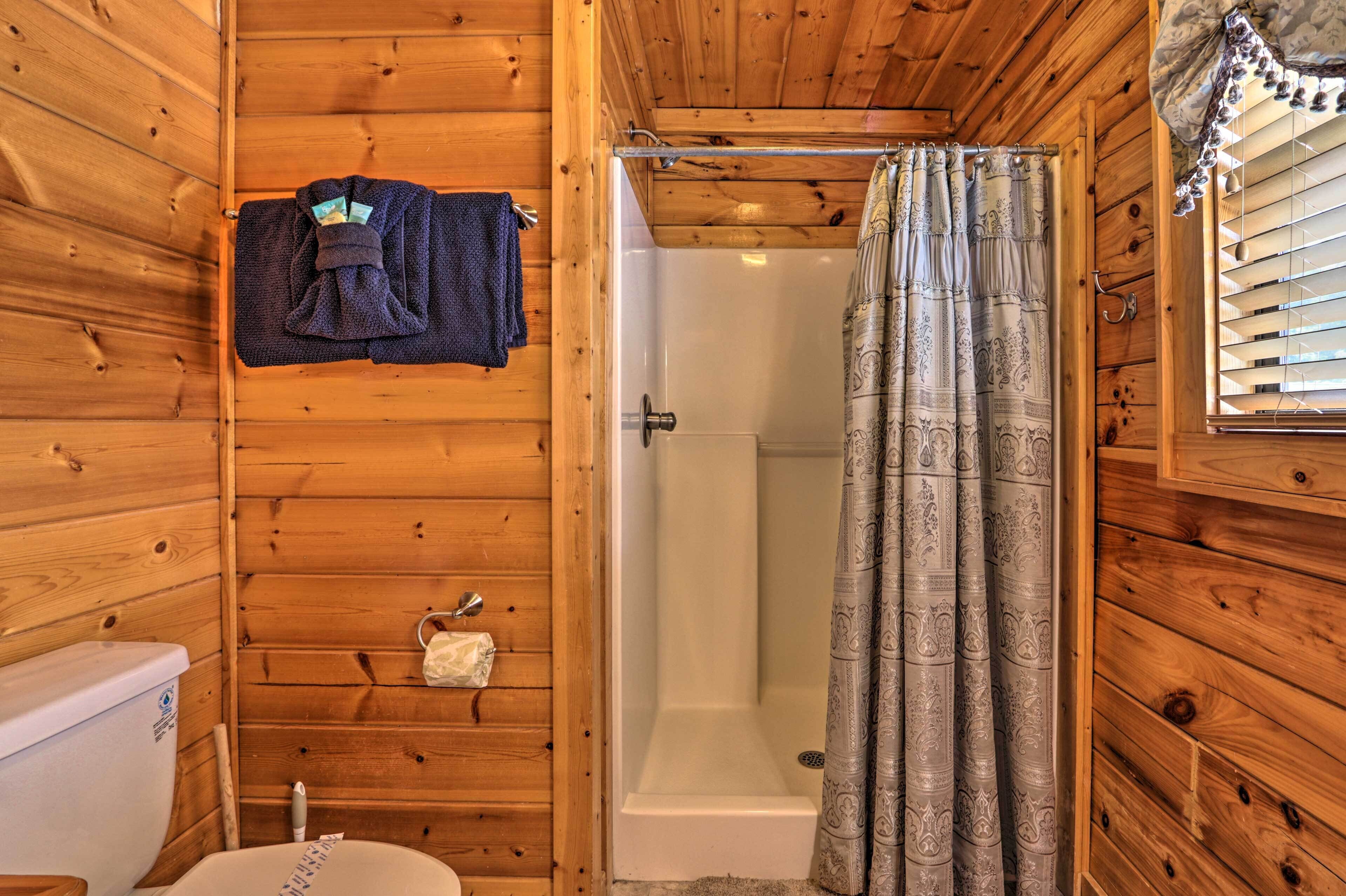 A wooden cabin bathroom with a shower, toilet, and towel rack.
