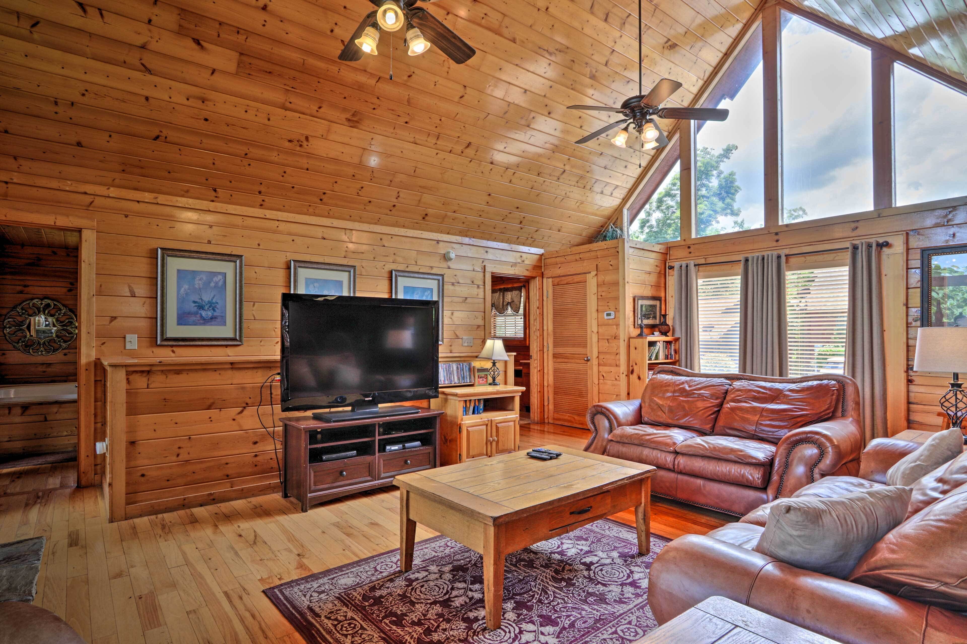 A wooden interior with a television, leather sofa, and a ceiling fan.