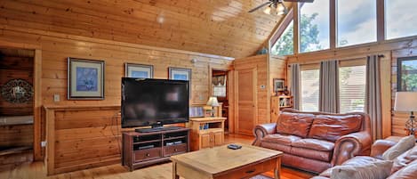 A wooden interior with a television, leather sofa, and a ceiling fan.