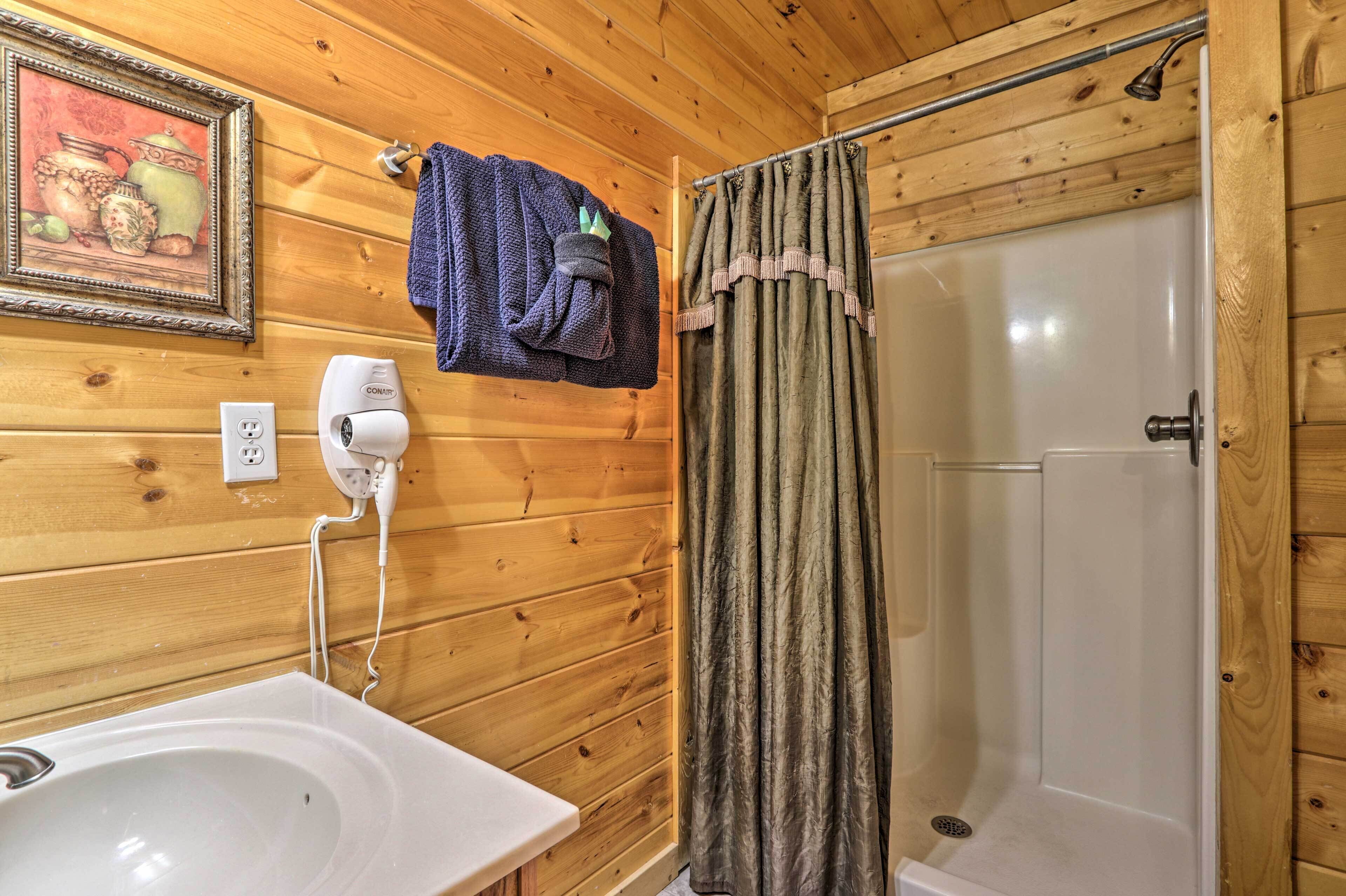A wooden-paneled bathroom with a sink, a towel rack with a towel, a hairdryer, and a shower curtain.